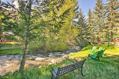 two park benches sitting in the grass near a stream at Chicago Creek B and B 1 Mi to Mt Blue Sky! in Idaho Springs