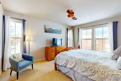 a bedroom with a bed and a chair and windows at Sagebrush Cabin in Granby