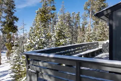 a wooden bench on a deck with snow covered trees at 59 Jabberwocky Home by Stay Winter Park in Fraser