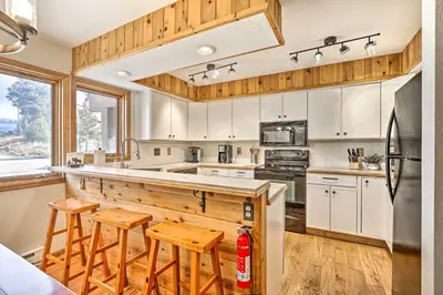a kitchen with white cabinets and a counter with stools at Sunny Alpine Escape with Hot Tub and Mountain Vistas! in Fraser