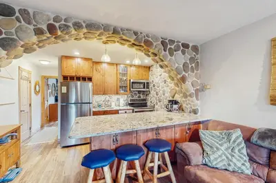 a kitchen with a large stone wall and blue stools at Hi Country Haus 14-5 in Winter Park