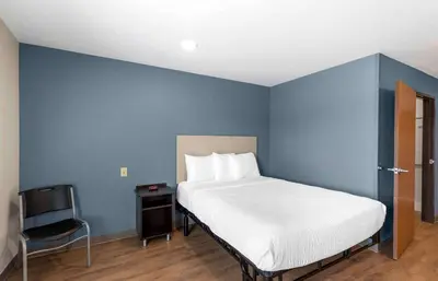 a blue bedroom with a bed and a chair at Extended Stay America Select Suites - Firestone in Firestone