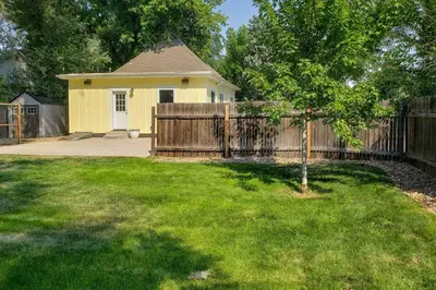 a yellow house with a wooden fence and a yard at Contemporary Longmont Hideaway in Old Town! in Longmont
