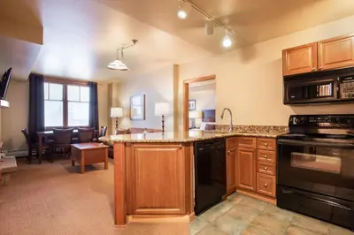 a kitchen with wooden cabinets and a living room at Ski-In Ski-Out Cozy 4th Floor Zephyr Mountain Lodge Condo Tucked Into The Woods condo in Winter Park