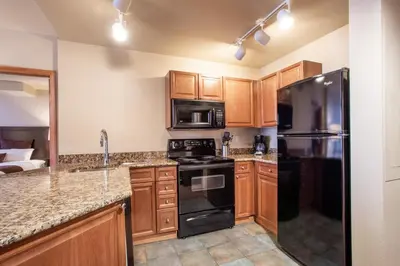 a kitchen with wooden cabinets and a black refrigerator at Ski-In Ski-Out Cozy 4th Floor Zephyr Mountain Lodge Condo Tucked Into The Woods condo in Winter Park