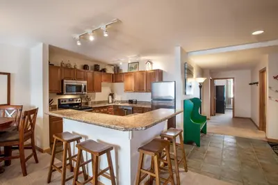 a kitchen with wooden cabinets and a counter with bar stools at Roomy Zephyr Mountain Lodge Condo with Perfect Slope View from Balcony condo in Winter Park