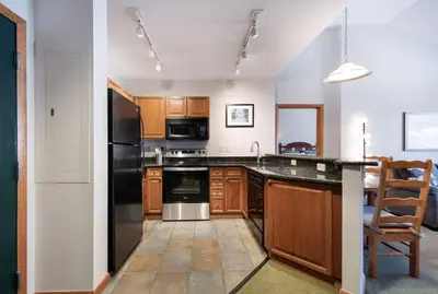 a kitchen with wooden cabinets and a black refrigerator at Comfortable Mountain Adventure Condo at Zephyr Mountain Lodge with Village View condo in Winter Park