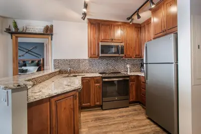 a kitchen with wooden cabinets and a stainless steel refrigerator at Cozy Lower Hughes View 2 BR Zephyr Mountain Lodge Condo with Ski Storage condo in Winter Park
