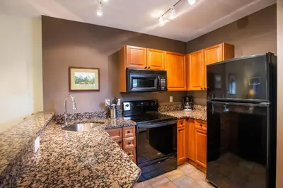 a kitchen with wooden cabinets and a black refrigerator at Unique & Comfortable Zephyr Mountain Lodge Condo with Slope and Continental Divide View condo in Winter Park