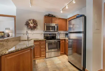 a kitchen with wooden cabinets and a stainless steel refrigerator at Great Ski-In Ski-Out Zephyr Mountain Lodge Condo with Lovely Balcony Views condo in Winter Park