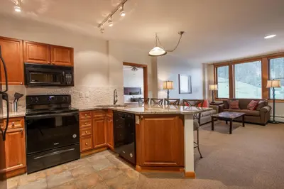 a kitchen with wooden cabinets and a living room at Remodeled Zephyr Mountain Lodge condo with upgraded furnishings and Slope Side View condo in Winter Park
