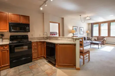 a kitchen with black appliances and a living room at Spectacular Zephyr Mountain Lodge Condo with Ski Slope View condo in Winter Park
