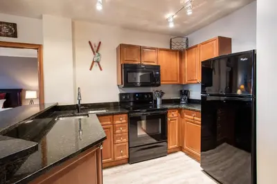 a kitchen with black appliances and wooden cabinets at Terrific Zephyr Mountain Lodge Condo With Beautiful Views of the Continental Divide near Mountain condo in Winter Park