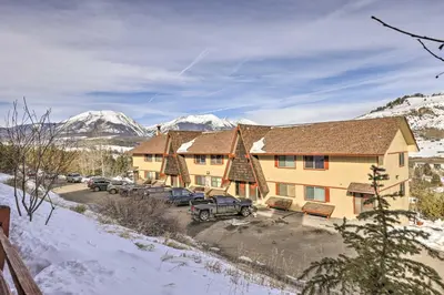 a building with cars parked in a parking lot with snowy mountains at Steps to Dillon Reservoir Mtn-View Condo in Dillon
