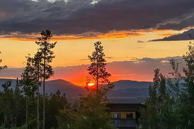 a sunset over the mountains with trees and a house at Pine Peak in Fraser