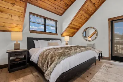a bedroom with a large bed and two windows at Brand NEW Located on Lake Estes Private Jacuzzi Two Patios Indoor and Outdoor Fireplace in Estes Park
