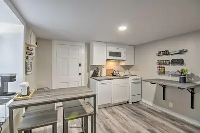 a small kitchen with white cabinets and a table at Fresh Downtown Longmont Apartment - Walk to Main! in Longmont