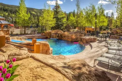 a pool in a backyard with chairs and rocks at Beautiful 3 Bedroom Mountain Condo In River Run Village With Hot Tub Access And Walking Distance To The Gondola in Keystone