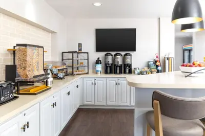 a kitchen with white cabinets and a tv on the wall at Staybridge Suites Denver - Central Park by IHG in Denver