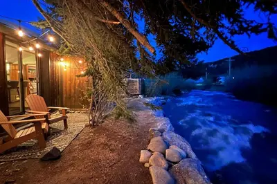 a house with a bench next to a river at night at Thorpe On The Water. Creekside Nederland Cabin. in Nederland