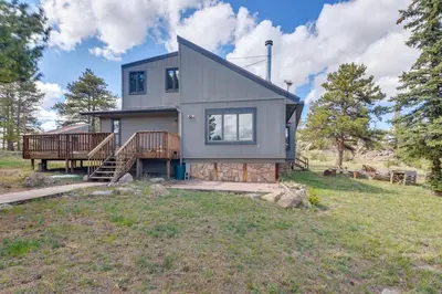 a house on a grassy field with trees at Cozy Red Feather Lakes Retreat with Deck and Yard in Red Feather Lakes