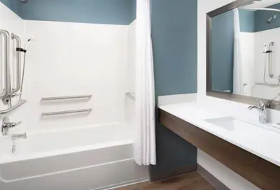 a bathroom with a tub and a sink and a mirror at WoodSpring Suites Littleton-South Denver in Littleton