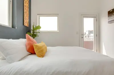 a white bed with orange and yellow pillows on it at Modern Denver Townhome with Rooftop Terrace! in Denver