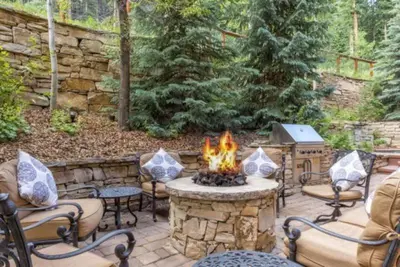 a stone patio with a fire pit with chairs and a fire at The Timbers In River Run 2 Bedroom Condo in Dillon