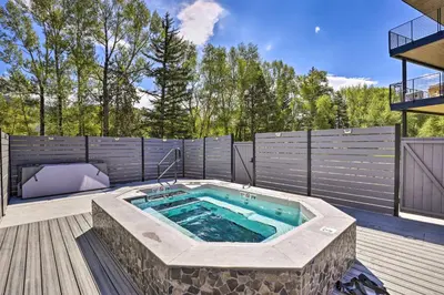 a hot tub in a patio with a fence and trees at Hot Tub and Balcony Riverfront Silverthorne Condo! in Silverthorne