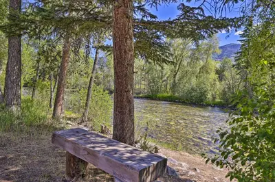 a wooden bench sitting next to a tree next to a river at Hot Tub and Balcony Riverfront Silverthorne Condo! in Silverthorne