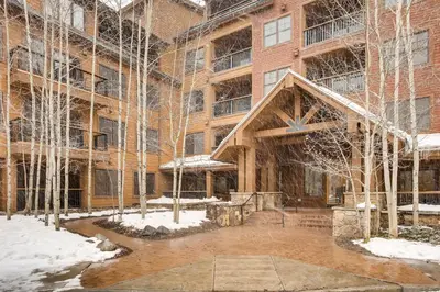 a large brick building with snowcovered trees in front of it at The Springs Condominiums by Vail Resorts in Keystone