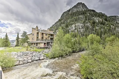 a building next to a river in front of a mountain at Main Street Frisco Condo with Private Patio! in Frisco