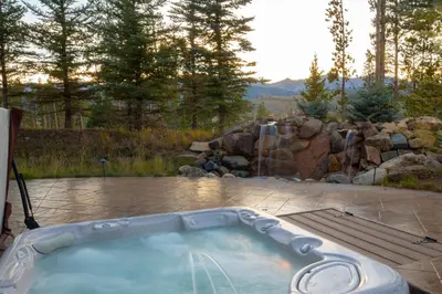 a jacuzzi tub in a backyard with a rock wall at Four master suites, VIEWS!! Hot tub, private ski SHUTTLE, sprawling entertaining areas!! in Breckenridge