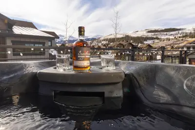 a bottle of whiskey and glasses sitting on a table at Modern Elegance, Stunning Mountain Views, Hot Tub, Fire Pit, Walk to River! in Breckenridge