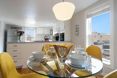 a dining room with a glass table and yellow chairs at Pine Street Loft Steps from Old Town Square in Fort Collins