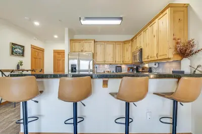 a kitchen with wooden cabinets and bar stools at Winter Park Condo with Balcony and Mtn Views! in Winter Park