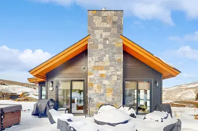 a house with a stone chimney and chairs in the snow at A Slice of Silverthorne in Silverthorne