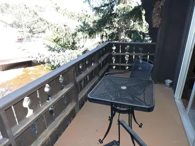 a table and chair on a porch with a fence at Elkhorn One Bedroom Condo with River View from Deck and Walking Distance to Estes Park - #3262 in Estes Park
