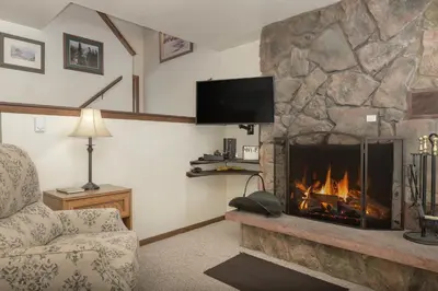 a living room with a stone fireplace with a tv at Hideaway Village Alpine 4 in Winter Park