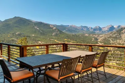 a table and chairs on a deck with a view of mountains at Moose Den Luxury Vacation Home at Windcliff home in Estes Park