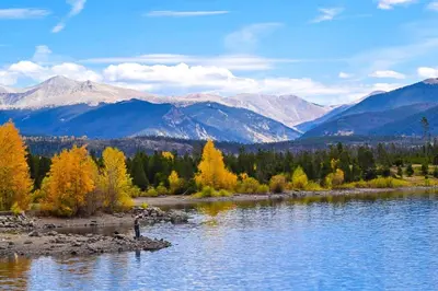 a person standing on the shore of a river with mountains at Sail Lofts at Lake Dillon 304 in Dillon