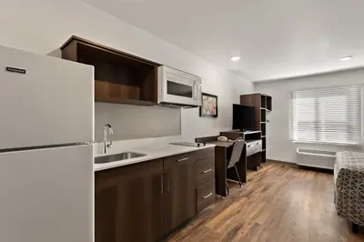 a kitchen with a white refrigerator and wooden floors at WoodSpring Suites Fort Collins in Fort Collins