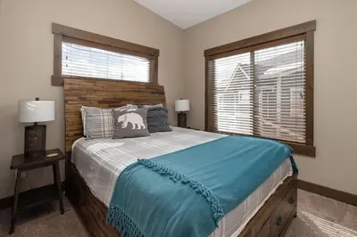 a bedroom with a bed with a wooden headboard and two windows at Mountain Haus home in Fraser